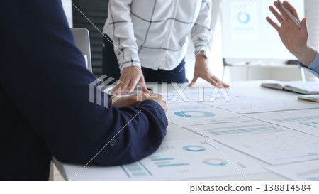 Business team discussing financial charts and strategy with graphs and data analysis documents on office desk during meeting for planning and corporate decisions Business team discussing financial charts and strategy with graphs and data analysis documents on office desk during meeting for planning and corporate decisions 138814584