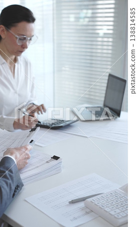 Professionals handling a large stack of documents and paperwork, signing a contract in a busy office. Audit and taxes in business Professionals handling a large stack of documents and paperwork, signing a contract in a busy office. Audit and taxes in business 138814585