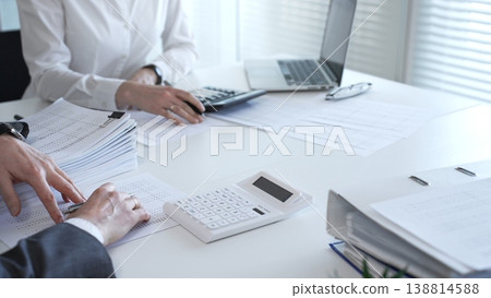 Professionals examining financial data and stacks of paperwork, performing a thorough audit and detailed investigation. Audit and taxes in business Professionals examining financial data and stacks of paperwork, performing a thorough audit and detailed investigation. Audit and taxes in business 138814588