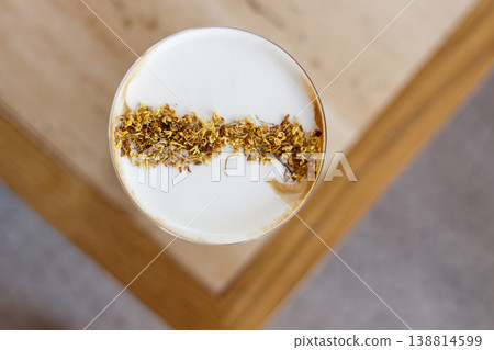 Cup of creation coffee drink and milk foam decorated with Osmanthus flower on wooden table by the window. 138814599