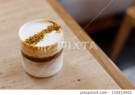 Cup of creation coffee drink and milk foam decorated with Osmanthus flower on wooden table by the window. 138814602