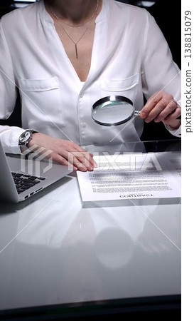 Businesswoman analyzing contract text with magnifying glass, scrutinizing fine print for legal details and agreement review. Audit, business concepts 138815079