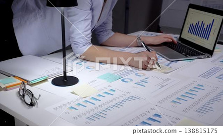 Professional woman analyzing financial data and business reports on a digital tablet in a dimly lit office, managing corporate strategy and market trends late at night 138815175