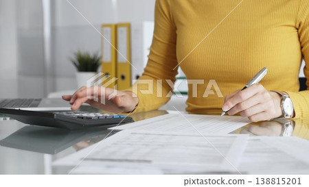 Woman calculating budget and reviewing financial documents using a laptop and calculator for home finances. Audit and taxes in business Woman calculating budget and reviewing financial documents using a laptop and calculator for home finances. Audit and taxes in business 138815201