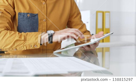 Person using a digital tablet for business at desk, navigating online content or browsing documents. Audit and taxes in business Person using a digital tablet for business at desk, navigating online content or browsing documents. Audit and taxes in business 138815297