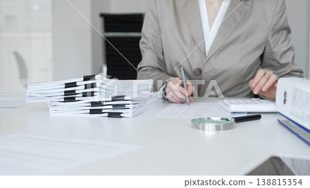 Businesswoman reviewing financial reports, calculating taxes, and managing audit paperwork in a busy office setting. Audit and taxes concept Businesswoman reviewing financial reports, calculating taxes, and managing audit paperwork in a busy office setting. Audit and taxes concept 138815354