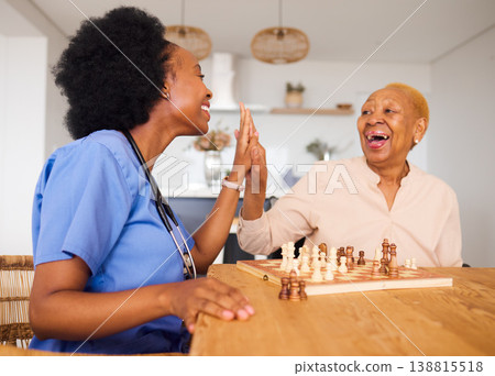 Caregiver playing chess with an elderly patient after healthcare consultation in nursing rehabilitation center. Board game, high five and female nurse bonding with senior woman in retirement home. Caregiver playing chess with an elderly patient after healthcare consultation in nursing rehabilitation center. Board game, high five and female nurse bonding with senior woman in retirement home. 138815518
