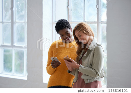 Friends, smartphone and communication, women and smile at chat, scroll social media during work break. Diversity, mobile app and female people using phone, young professional team and meme online Friends, smartphone and communication, women and smile at chat, scroll social media during work break. Diversity, mobile app and female people using phone, young professional team and meme online 138816101