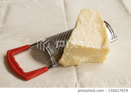 Piece of hard parmesan cheese with metal grater on white cloth Piece of hard parmesan cheese with metal grater on white cloth 138817659