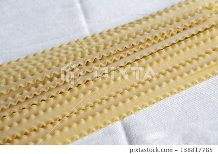 Raw Mafaldine pasta ribbons on white linen cloth. Traditional Italian wavy pasta pattern. Uncooked organic durum wheat Reginette noodles texture. Top view with copy space. 138817785