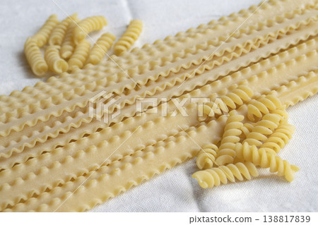 Assorted dry mafaldine and fusilli pasta on white linen tablecloth 138817839