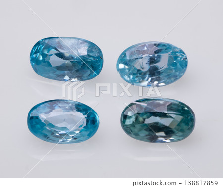 Four Oval Cut Light Blue Gemstones Arranged on a White Reflective Surface in Minimalist Style. Four Oval Cut Light Blue Gemstones Arranged on a White Reflective Surface in Minimalist Style. 138817859