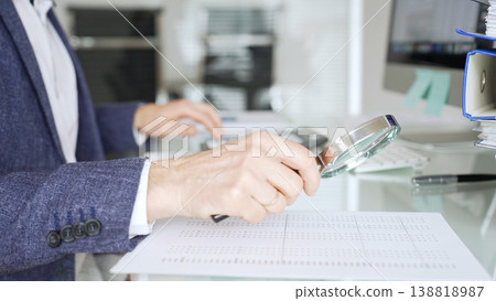 Auditor analyzing financial data with magnifying glass, scrutinizing business documents and accounting reports in office. Audit and taxes in business Auditor analyzing financial data with magnifying glass, scrutinizing business documents and accounting reports in office. Audit and taxes in business 138818987