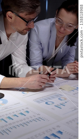 Business colleagues collaborating on financial reports, analyzing market data and corporate strategy by reviewing charts and graphs on a table in an office meeting 138818988