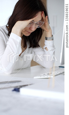 Stressed architect woman experiencing burnout and headache at office desk, tired from long hours working on computer. Business and architecture concept Stressed architect woman experiencing burnout and headache at office desk, tired from long hours working on computer. Business and architecture concept 138819031
