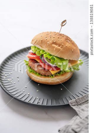 Beef burger with tomato, cheese, and lettuce on a black plate on a marble background with napkin Beef burger with tomato, cheese, and lettuce on a black plate on a marble background with napkin 138819081