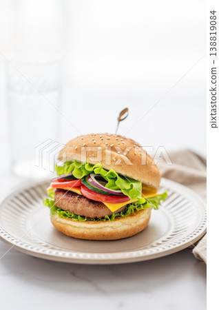 Beef burger with tomato, cheese, and lettuce on a plate on a marble table near window Beef burger with tomato, cheese, and lettuce on a plate on a marble table near window 138819084