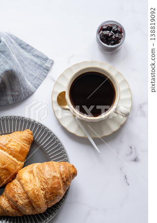 Freshly bakery croissants and cup of coffee on a light marble background with berry jam and spoon. Freshly bakery croissants and cup of coffee on a light marble background with berry jam and spoon. 138819092
