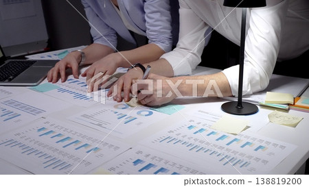 Business colleagues collaborating on financial reports and charts, analyzing data, discussing strategy, and preparing for an important meeting in a corporate office setting 138819200