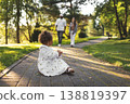 Cute mixed race toddler girl sitting on park path, interracial couple parents walking toward child in sunny green park, candid family lifestyle. Mom, dad and baby 138819397