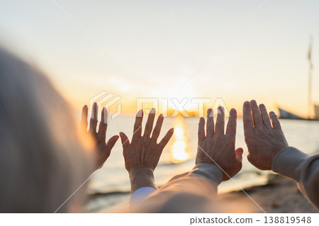 Senior couple hands at sunset. Old man woman pulls hand touching sun. Sunlight passing through fingers closeup shining sun. People stretching out hand to sun. Religion helping hand. Prayer in religion Senior couple hands at sunset. Old man woman pulls hand touching sun. Sunlight passing through fingers closeup shining sun. People stretching out hand to sun. Religion helping hand. Prayer in religion 138819548