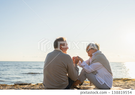 Senior mature couple sitting on beach holding hands enjoying outdoor recreation. Old husband wife touching hands with tenderness love. Grandmother grandfather together. Family moment of love Senior mature couple sitting on beach holding hands enjoying outdoor recreation. Old husband wife touching hands with tenderness love. Grandmother grandfather together. Family moment of love 138819554