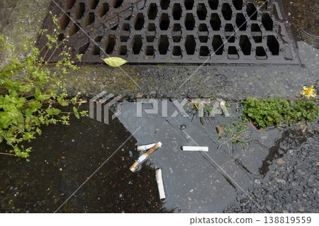 Cigarette butts discarded in a puddle near a drainage ditch Cigarette butts discarded in a puddle near a drainage ditch 138819559