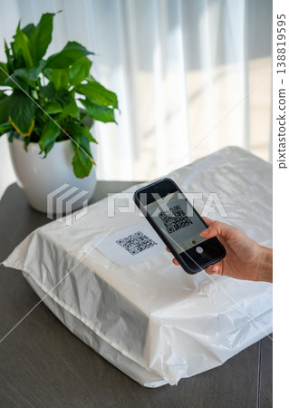 Person scanning QR code on parcel with smartphone camera for delivery tracking at home. Contactless technology mobile app and digital service concept. 138819595