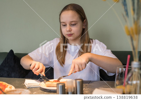 Cheerful young girl enjoying food. Child eating pizza in cafe 138819638
