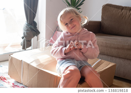 Curious 4 year old girl sitting on a huge delivery box and wondering what is inside 138819818