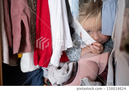 Little 4 Year Old Caucasian Girl Playing Hide-and-Seek Inside a Cluttered Clothes Wardrobe 138819824