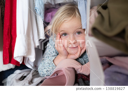 Little 4 Year Old Caucasian Girl Playing Hide-and-Seek Inside a Cluttered Clothes Wardrobe 138819827
