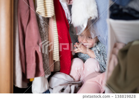 Little 4 Year Old Caucasian Girl Playing Hide-and-Seek Inside a Cluttered Clothes Wardrobe 138819828