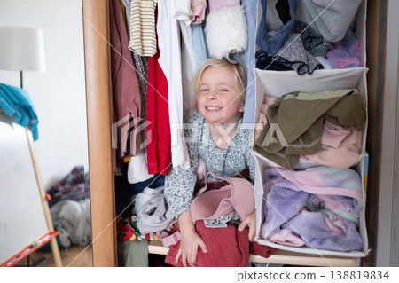 Little 4 Year Old Caucasian Girl Playing Hide-and-Seek Inside a Cluttered Clothes Wardrobe 138819834