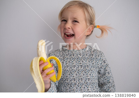 Healthy Snack Time: Charming 4 year old girl enjoying a fresh banana in a bright modern kitchen 138819840