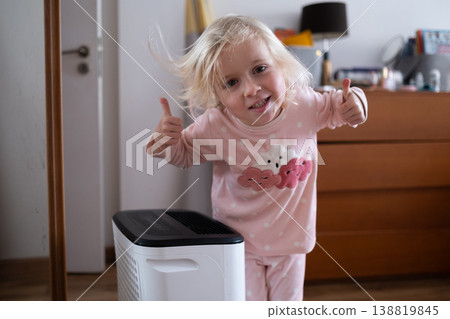Independent 4 year old girl turning on a modern air dehumidifier to control humidity in her room 138819845
