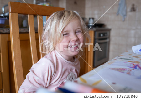 Joyful 4 year old girl smiling while sitting at a sunlit kitchen table in a cozy home Joyful 4 year old girl smiling while sitting at a sunlit kitchen table in a cozy home 138819846