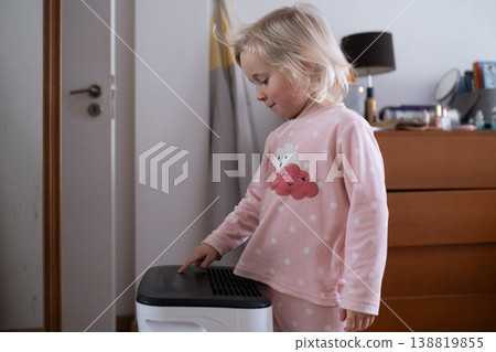 Independent 4 year old girl turning on a modern air dehumidifier to control humidity in her room 138819855