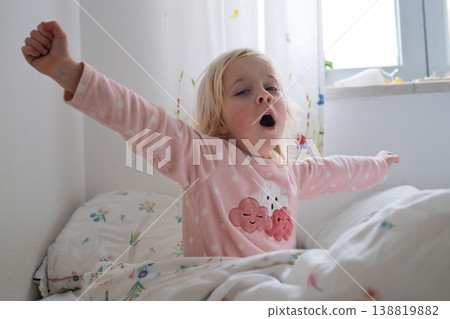 Adorable 4 year old girl yawning and stretching after waking up in a cozy sunlit bedroom Adorable 4 year old girl yawning and stretching after waking up in a cozy sunlit bedroom 138819882