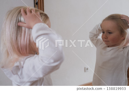 Funny little girl making faces in front of the mirror. 138819933
