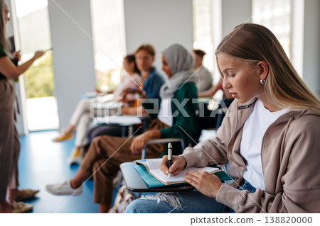 Female student writing notes during university lecture. Female student writing notes during university lecture. 138820000