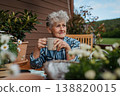 Senior woman with coffee sitting on terrace, resting after gardening. 138820015