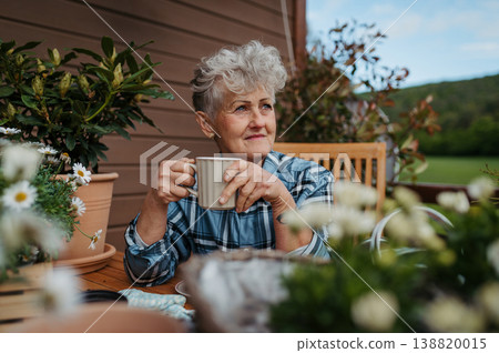 Senior woman with coffee sitting on terrace, resting after gardening. Senior woman with coffee sitting on terrace, resting after gardening. 138820015