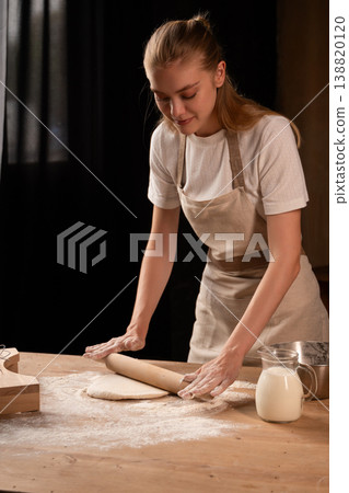 Young woman baking bread or pastry, rolling dough on a wooden table with flour, preparing food at home Young woman baking bread or pastry, rolling dough on a wooden table with flour, preparing food at home 138820120