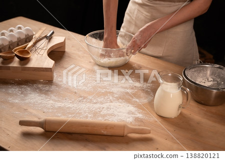 Person kneading dough for baking homemade bread on a rustic wooden table with flour, milk, and eggs Person kneading dough for baking homemade bread on a rustic wooden table with flour, milk, and eggs 138820121