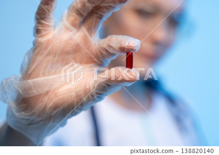 Hand in clear glove holding red medicine capsule, representing medical treatment and pharmaceutical research Hand in clear glove holding red medicine capsule, representing medical treatment and pharmaceutical research 138820140