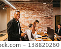 Man stands in office with papers while colleagues work at desks in a modern workplace environment 138820260