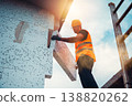 Worker installs building material on construction site during day near scaffold in bright sunlight 138820262