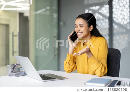Young businesswoman communicating enthusiastically on a mobile phone, sitting at a white desk with a laptop and notebook, showcasing her professional engagement and happy work environment Young businesswoman communicating enthusiastically on a mobile phone, sitting at a white desk with a laptop and notebook, showcasing her professional engagement and happy work environment 138820598