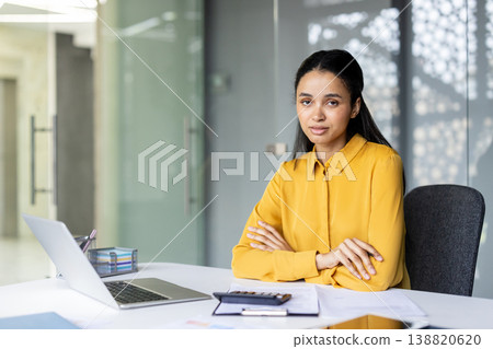 Young woman sitting at a desk with arms crossed, working in a contemporary office environment, embodying professionalism, entrepreneurship, and career success Young woman sitting at a desk with arms crossed, working in a contemporary office environment, embodying professionalism, entrepreneurship, and career success 138820620
